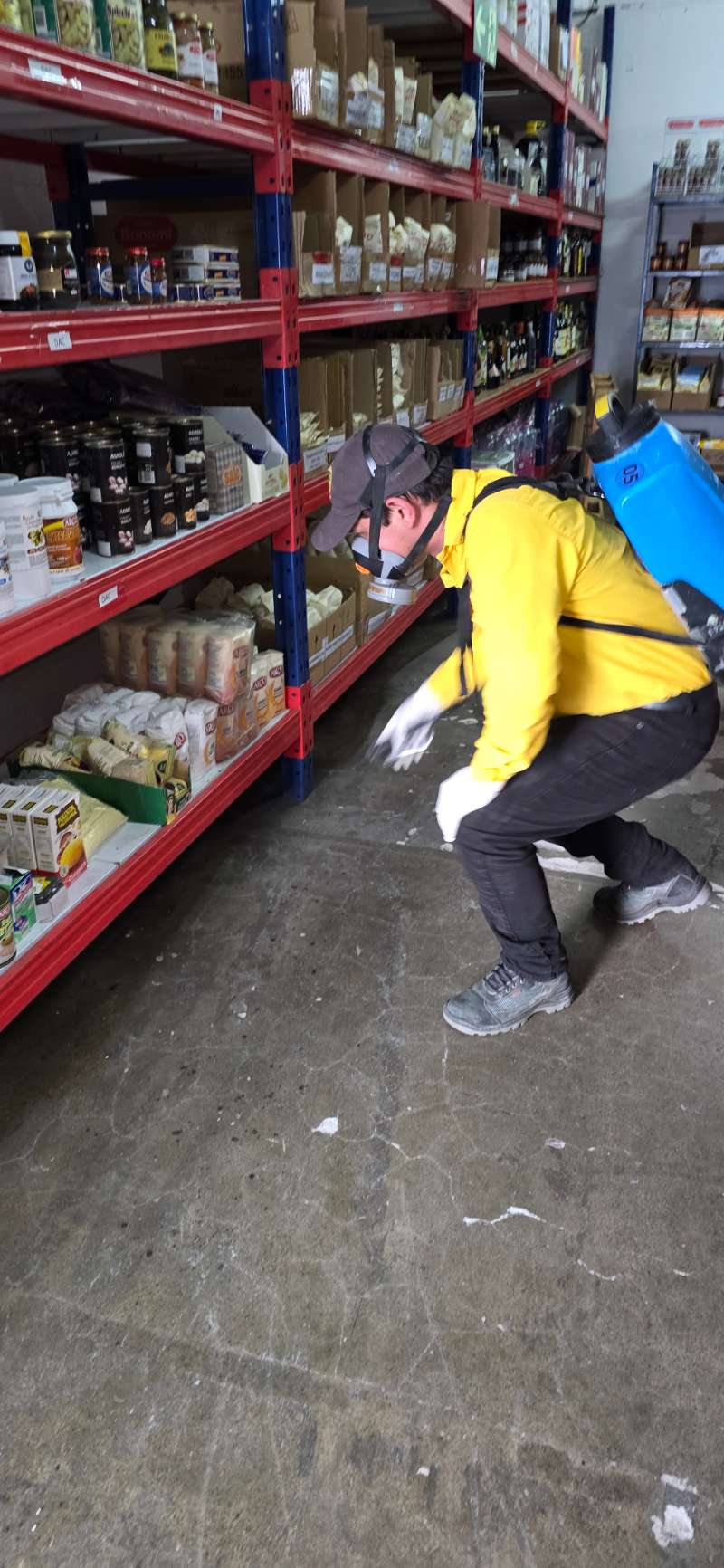 Técnico de EcoPlagas con respirador y uniforme aplicando tratamiento en un abastecedor