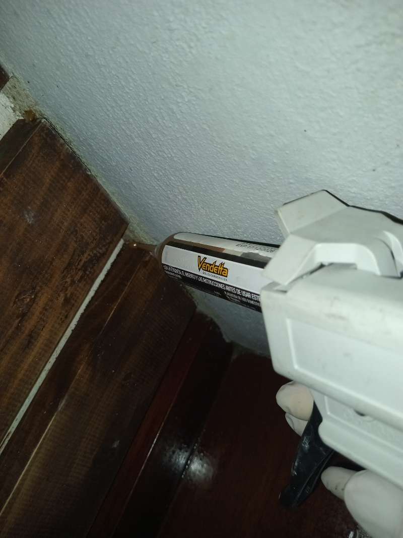 Pistola dosificadora profesional aplicando gel cucarachicida en la unión de pared y mueble